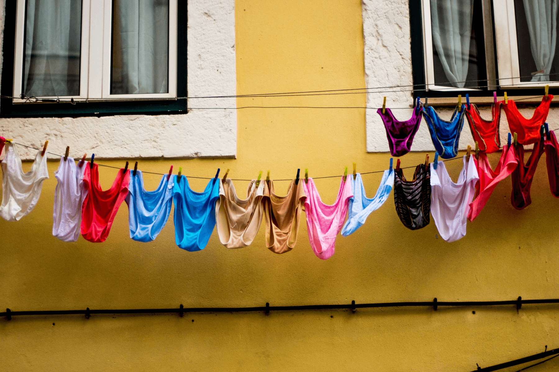 Many pairs of colorful underwear hang on a clothes line outside of a yellow building.