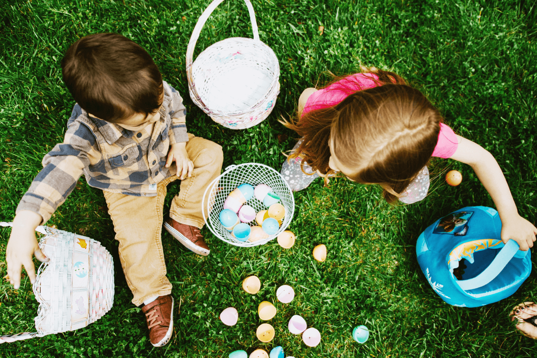 An overhead shot of two children in grass with Easter baskets and colorful plastic eggs.