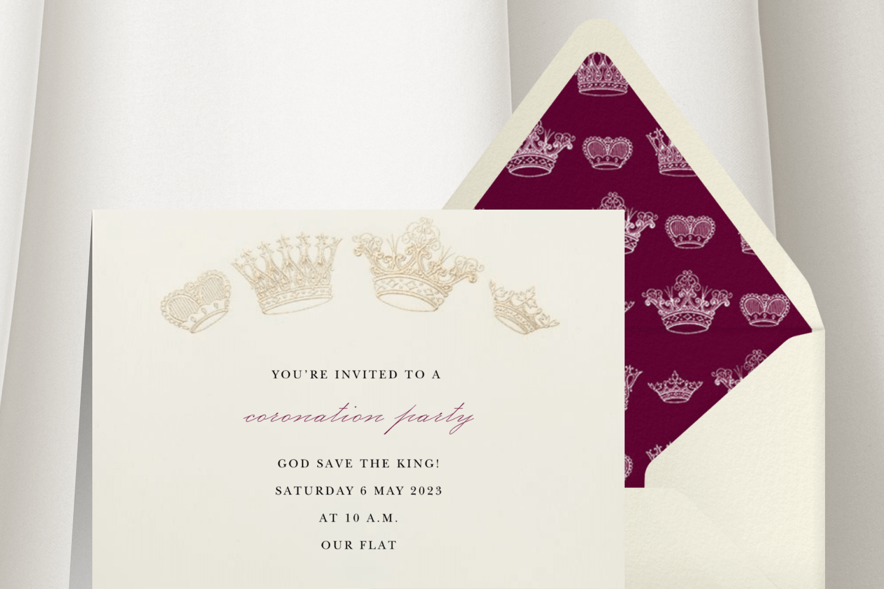 Alt text: A white invitation has four varying crowns in gold arched at the top, beside a white envelope with a maroon crown liner.