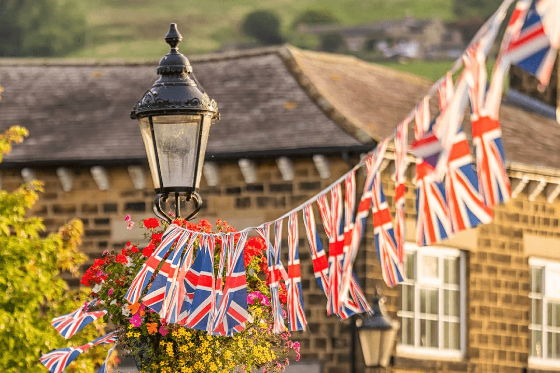 A string of Union Jack bunting flags hand from a lamppost in front of a brick building.