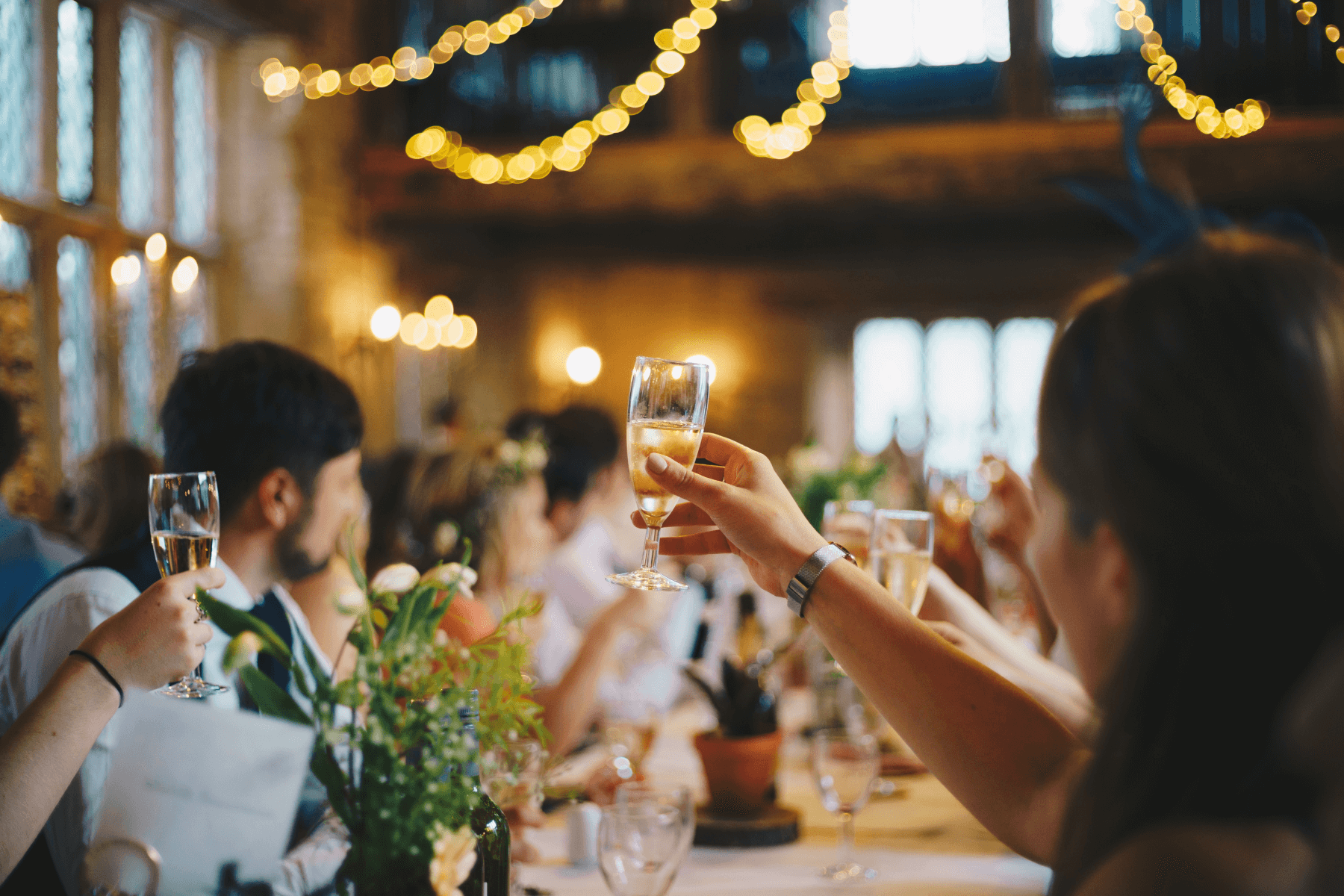 Soft focus shot of guests seated at a wedding and raising their glasses for a toast.
