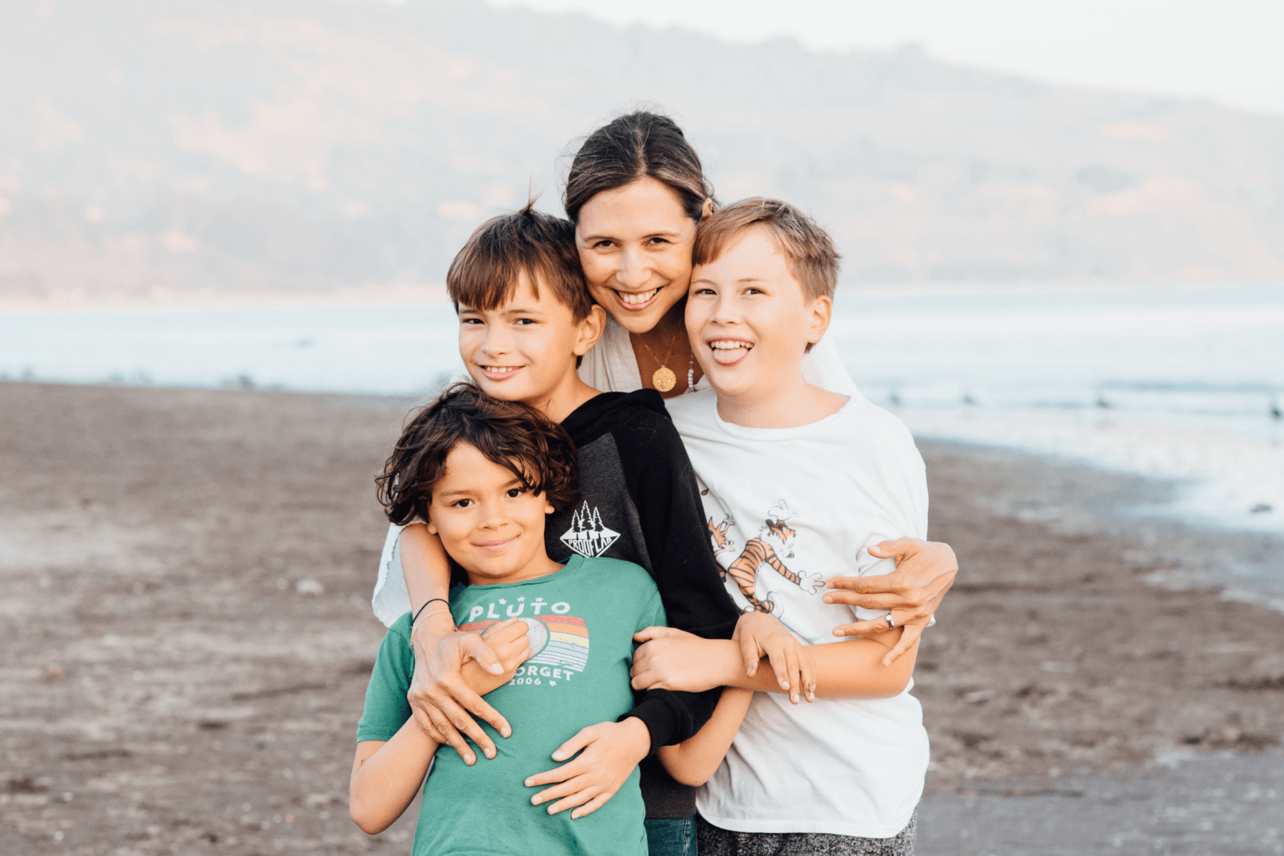 Sabrina Moyle hugging her three children on the beach.