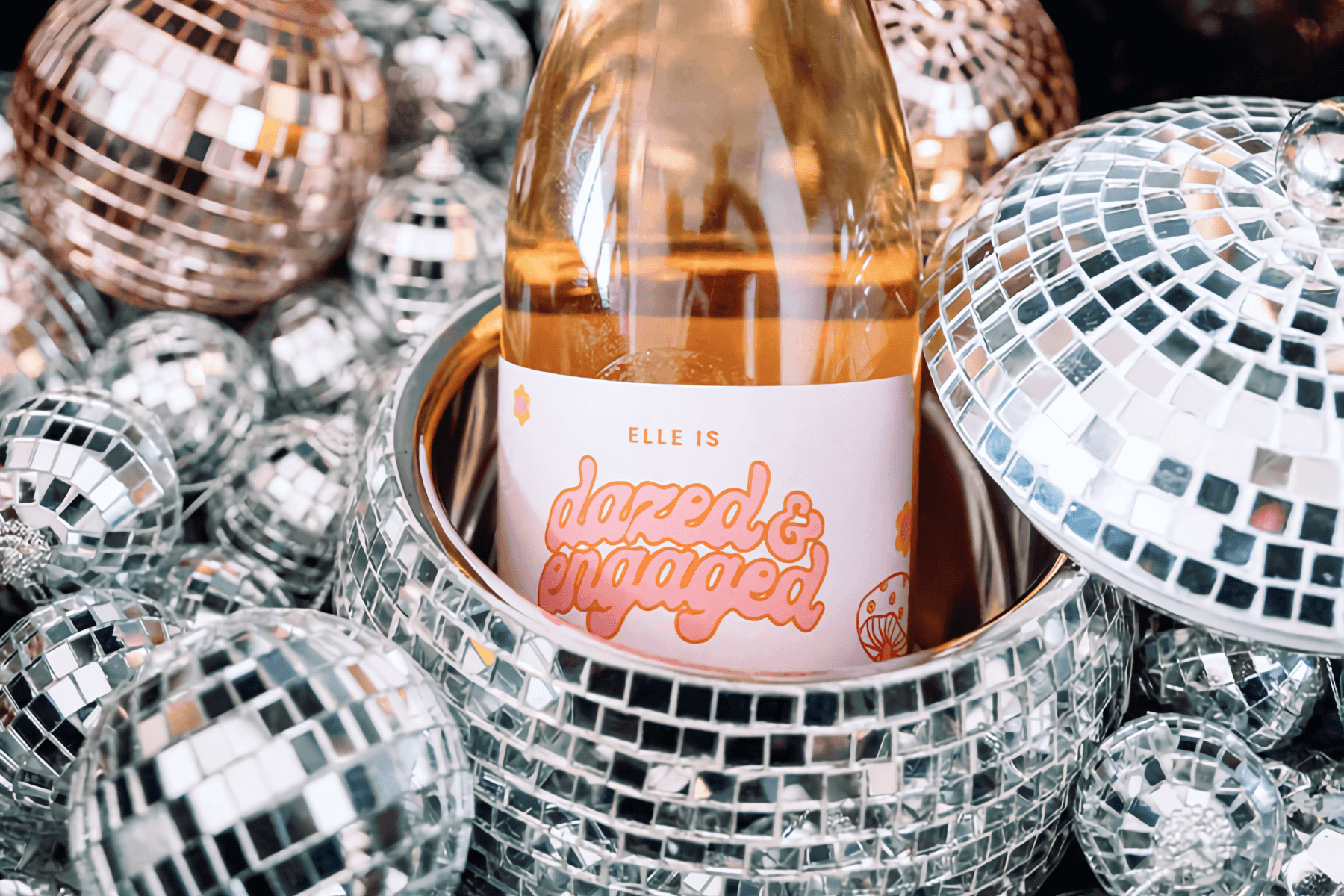 A bottle or rosé wine sits in an open disco ball surrounded by smaller disco balls.