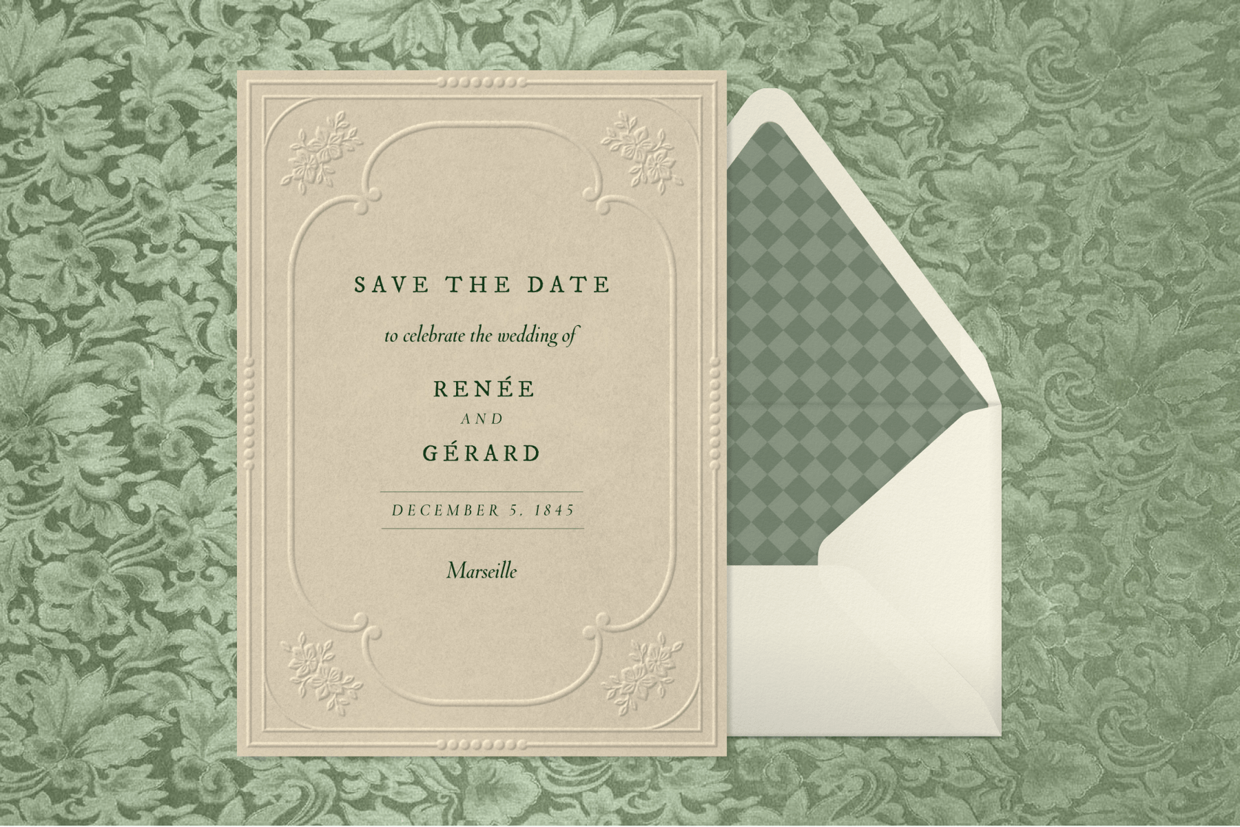 An ornate, embossed save the date invitation next to a cream-colored envelope with a checkered interior against a floral green backdrop.