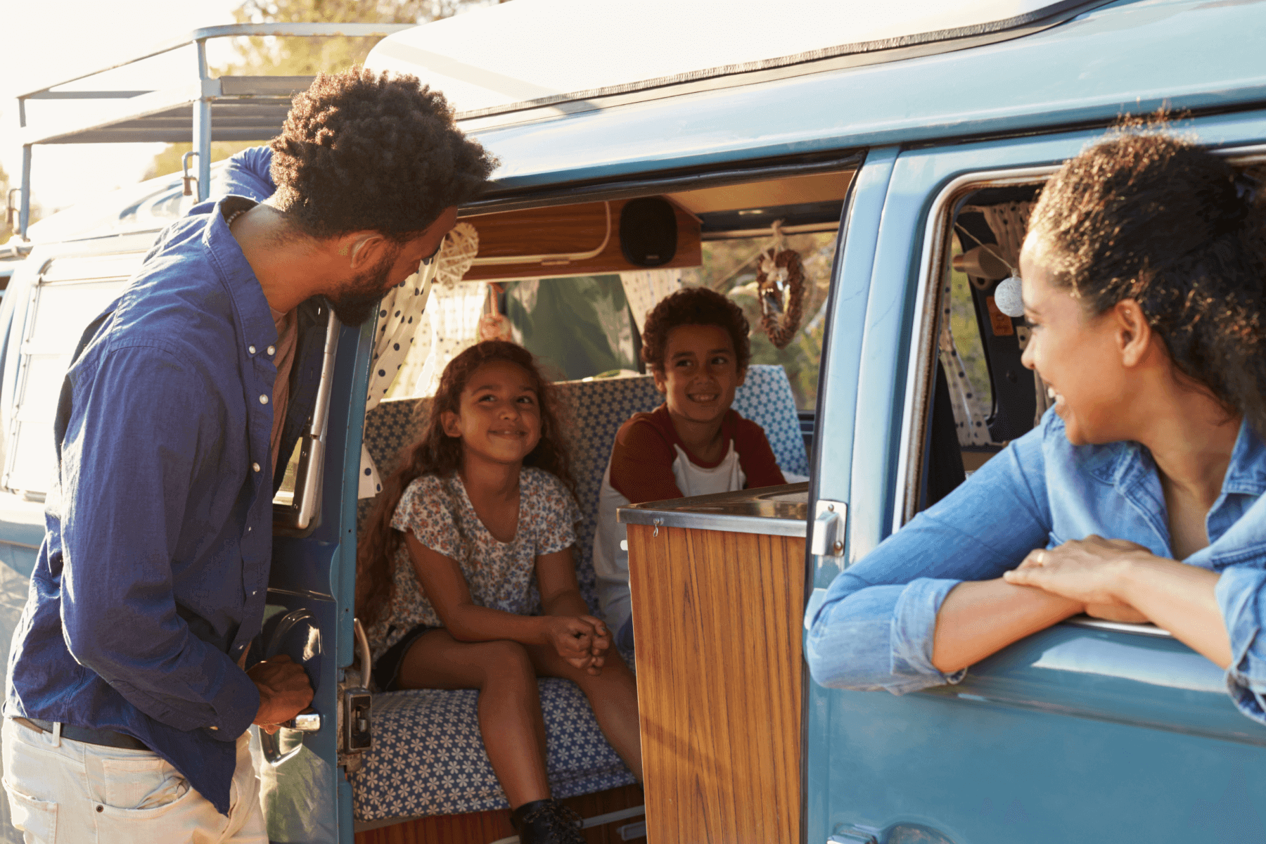 A mother and father smile at their two children in a vintage blue camper van.