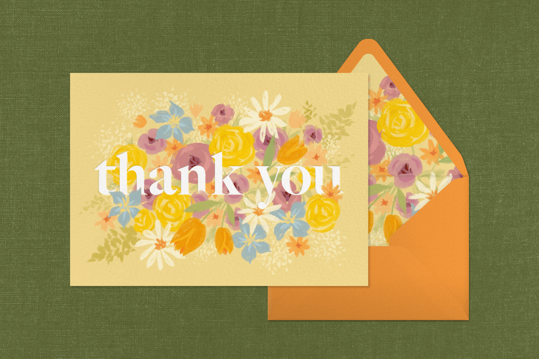 A floral thank you card on an orange envelope with a floral liner, set on a green fabric background. 