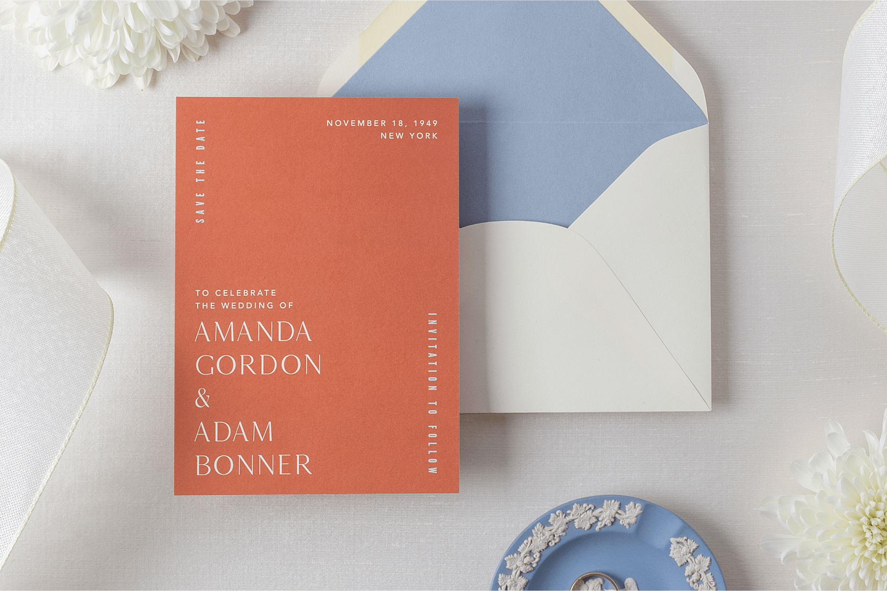 A salmon-colored save the date with white text with a white envelope with blue lining.