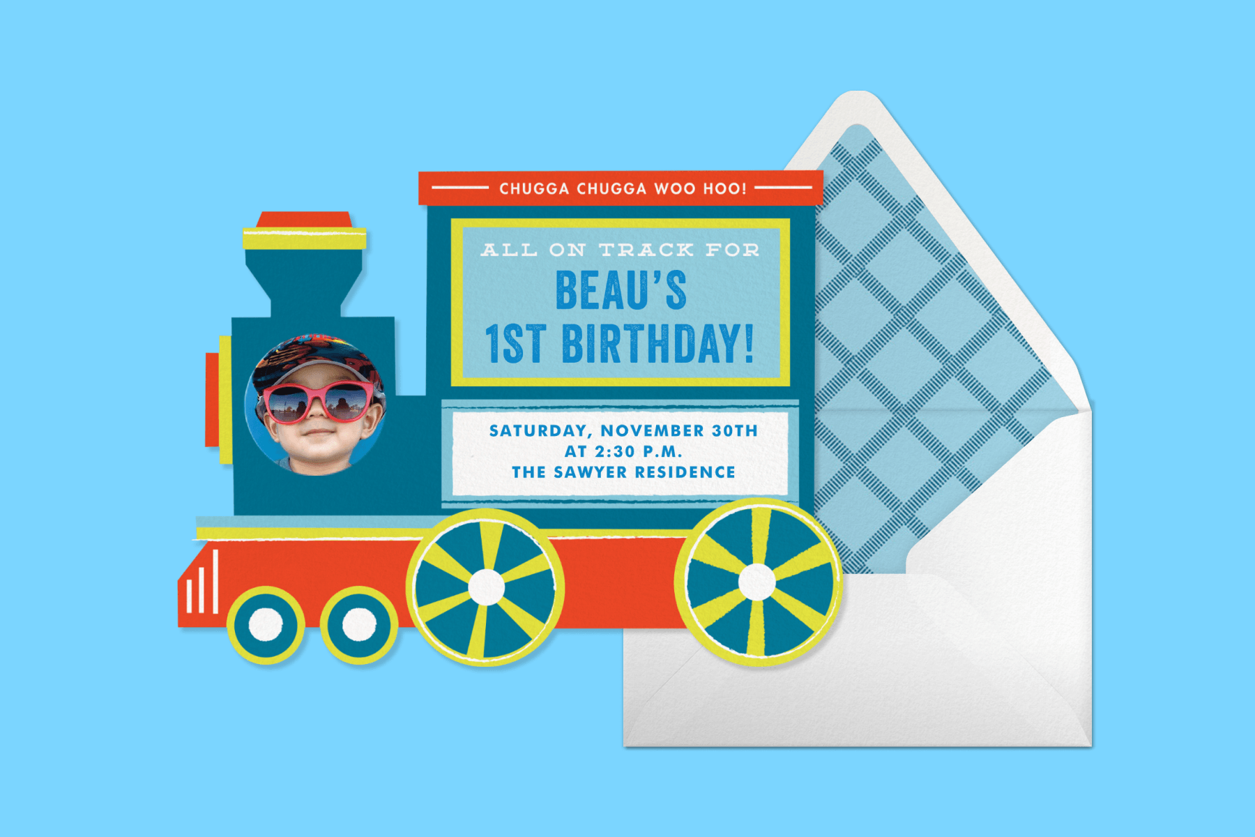 On a blue background, a train-shaped 1st birthday invitation featuring a photo of a child at the front of the train next to a white envelope with light and dark blue patterned lining. 