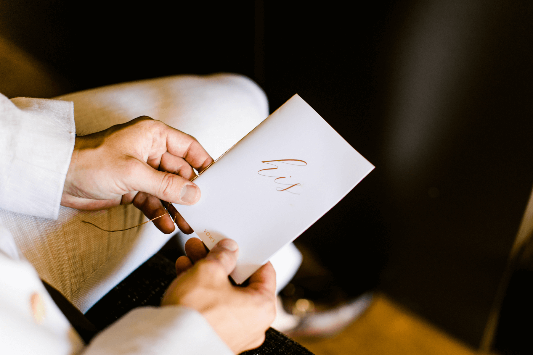 A person wearing a suit holding a card with calligraphy script that reads ‘his’