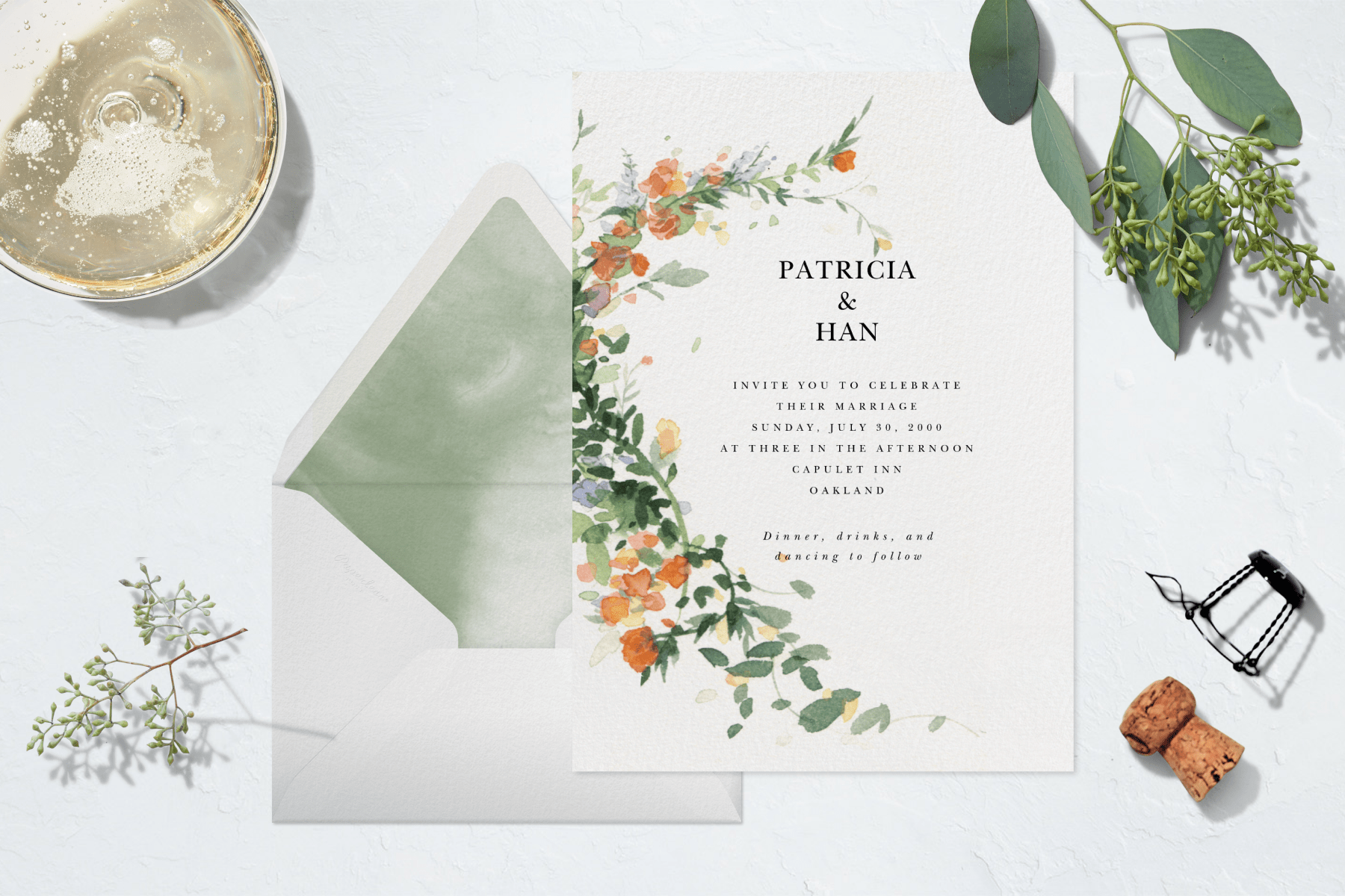 A wedding invitation with a watercolor leafy vine with orange and blue flowers on it, surrounded by a glass of sparkling wine and cork and two leafy twigs.