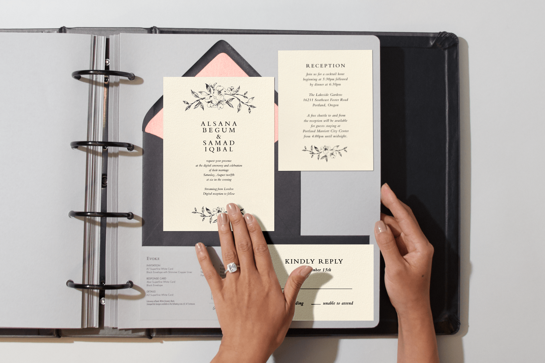 Two hands (one wearing an engagement ring) page through a binder with a wedding invitation featuring a line drawing of a flowering branch and matching details cards.