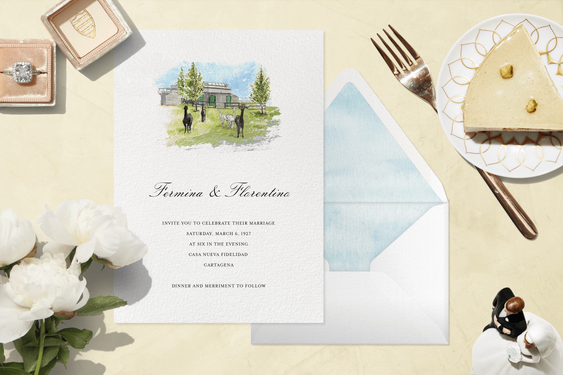 A wedding invitation with a watercolor painting of several black and white alpacas in front of a gray building. Beside it are white peonies, a diamond ring in a pink velvet box, a gold fork, a slice of pie on a plate, and a bride and groom cake topper.