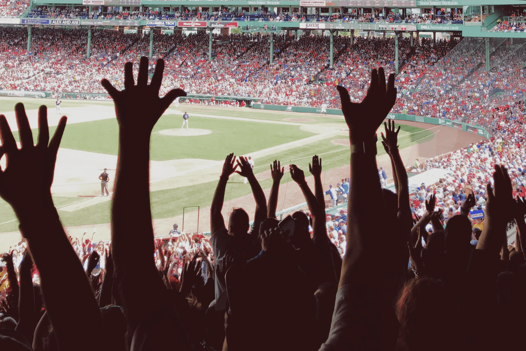 A view of people cheering at a baseball stadium from behind.
