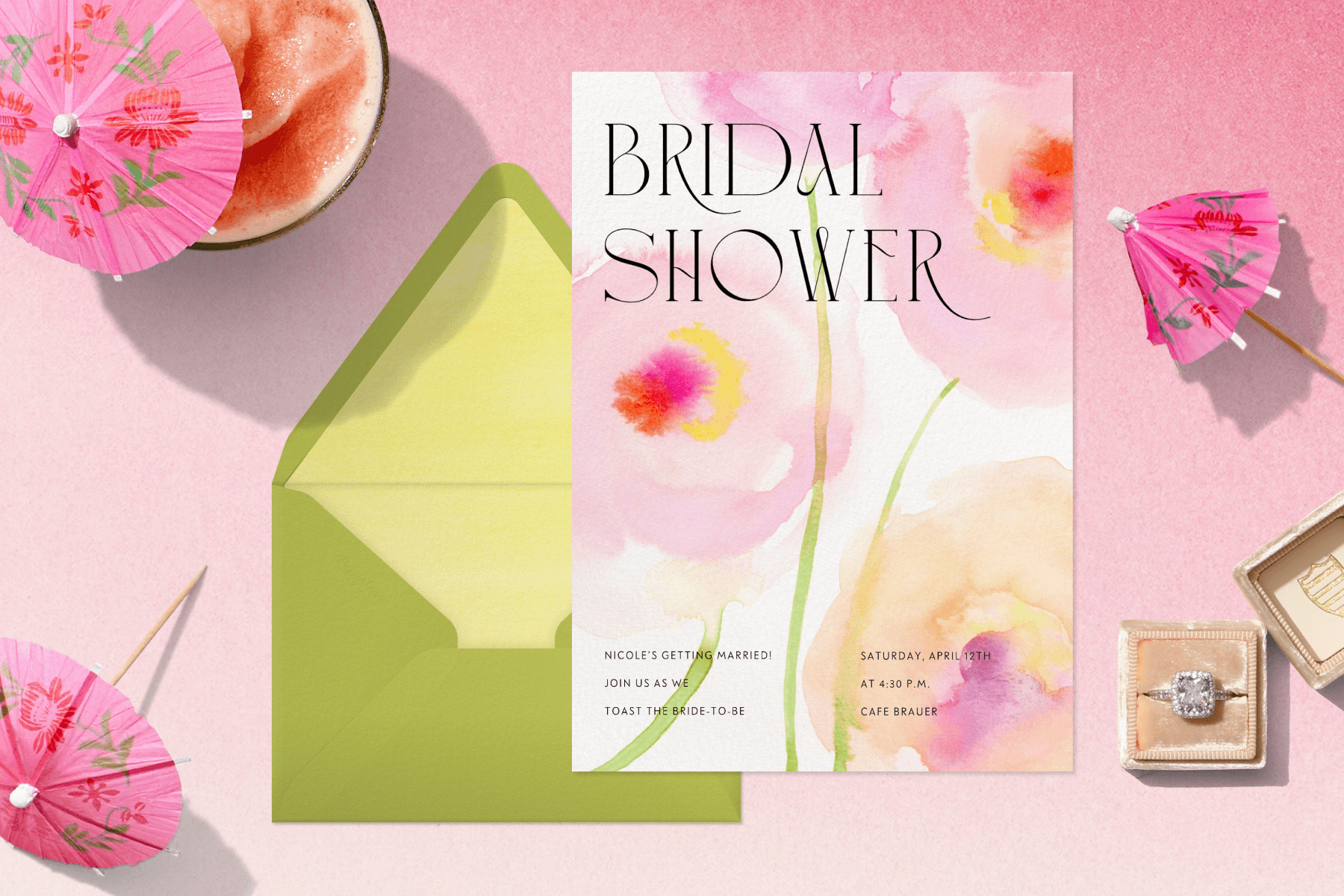 A pink watercolor bridal shower invitation surrounded by drink umbrellas and an engagement ring.