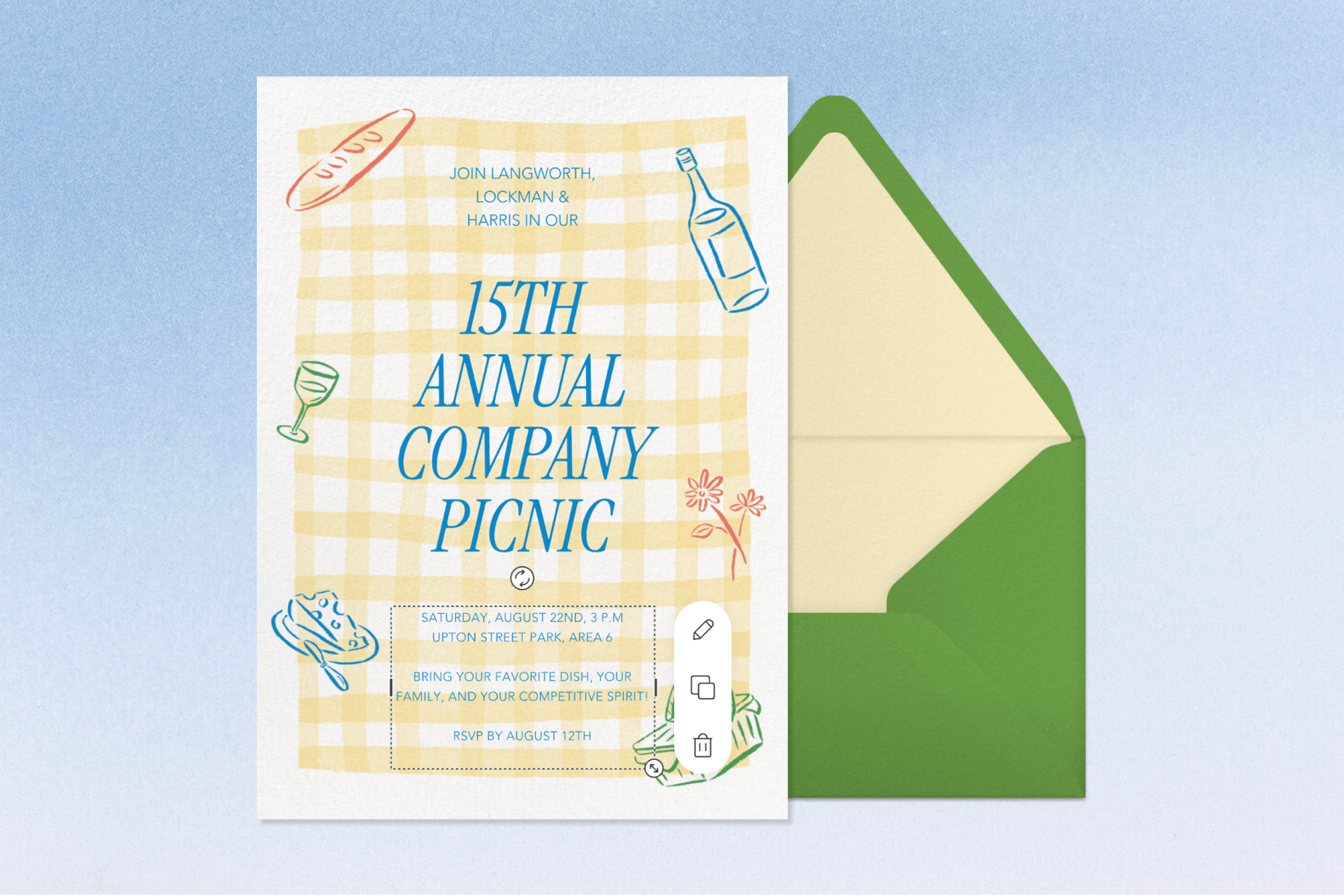 On a blue backdrop, a company picnic invitation with blue text on a yellow paisley pattern featuring illustrations of wine, bread, cheese, flowers, and a picnic basket. The invitation sits on a green envelope with yellow lining.