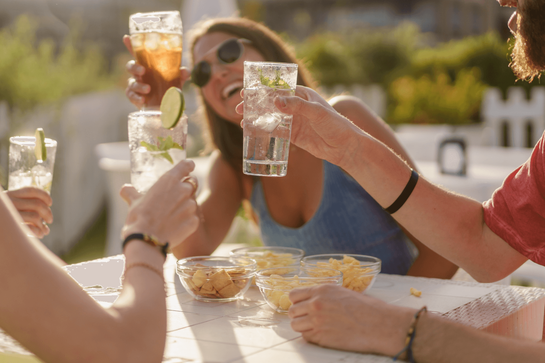 Several people toast with tall glasses outdoors over bowls of chips.