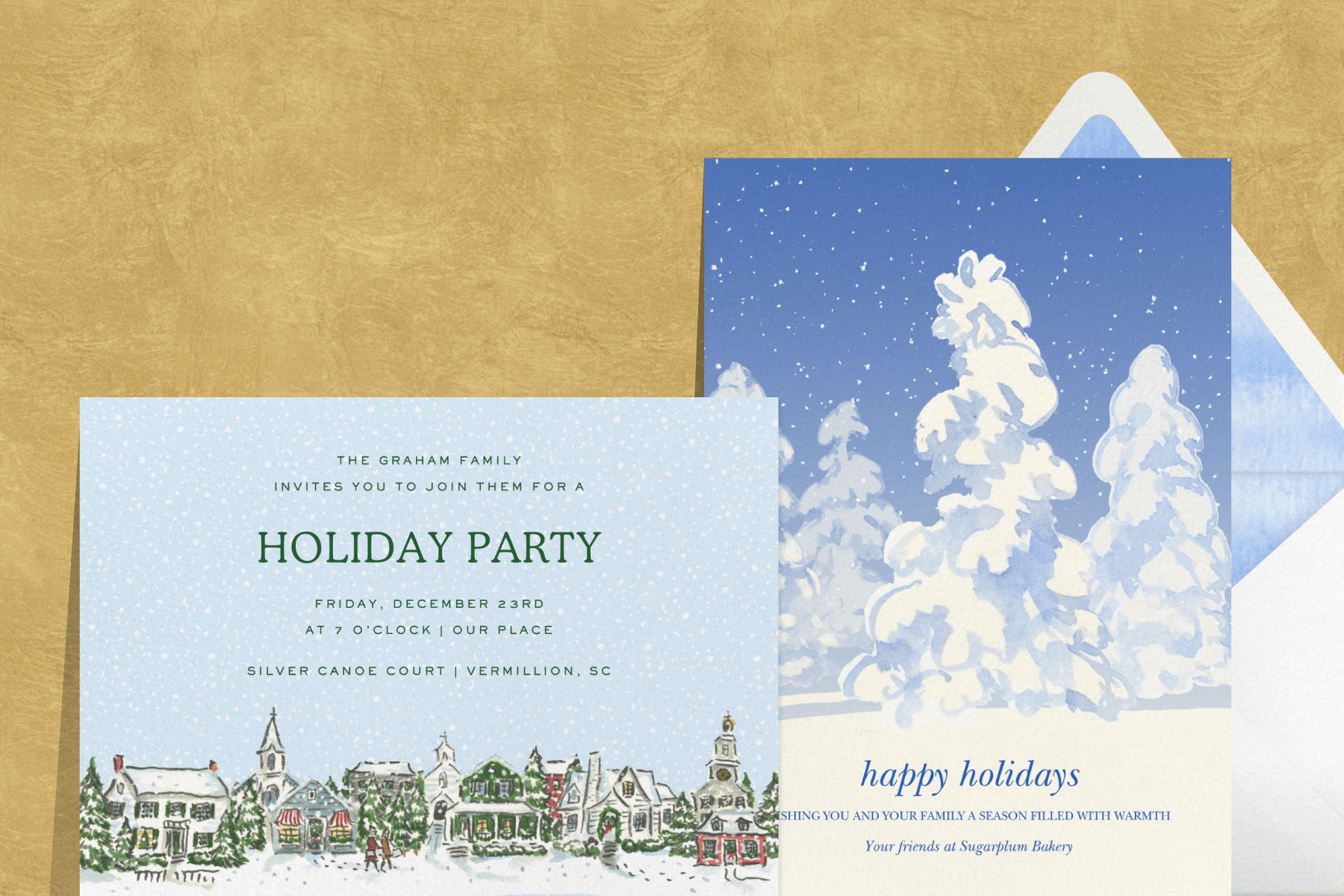 A gold textured background featuring two holiday cards: A holiday party invitation featuring a painted snowy scene of a row of houses; A holiday card featuring a blue and white snowy forest illustration paired with a white envelope and blue and white textured envelope liner.
