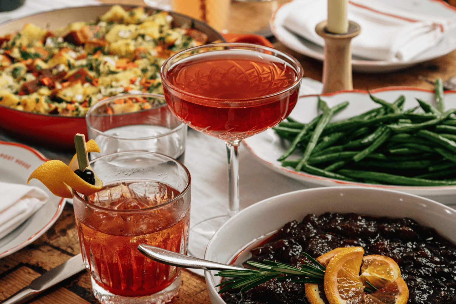 Glass of grapefruit gin and tonic on table with another drink, surrounded by stuffing, green beans, and cranberries. 