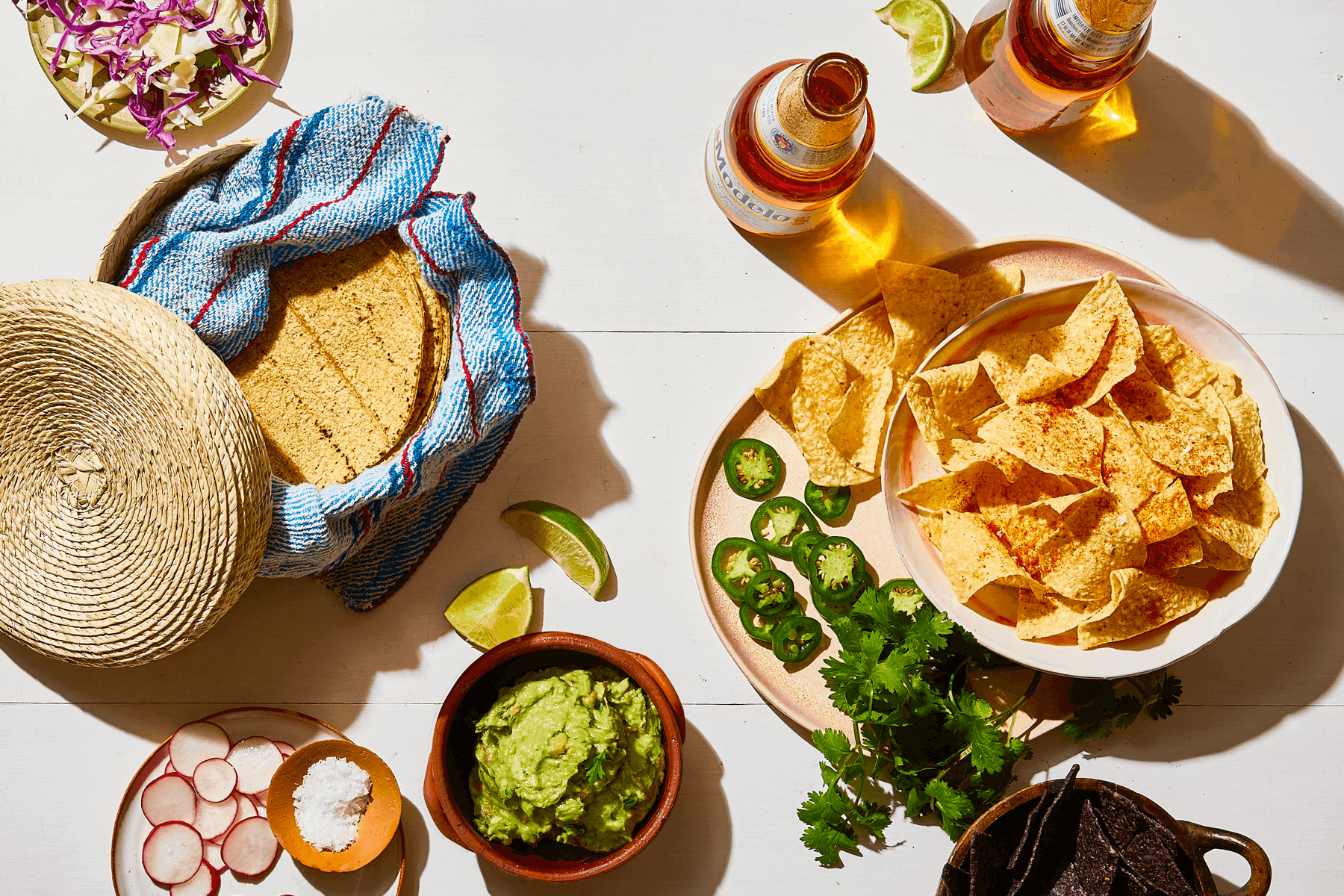 spread of Mexican finger food like tortillas, corn chips, peppers, guacamole, and beer