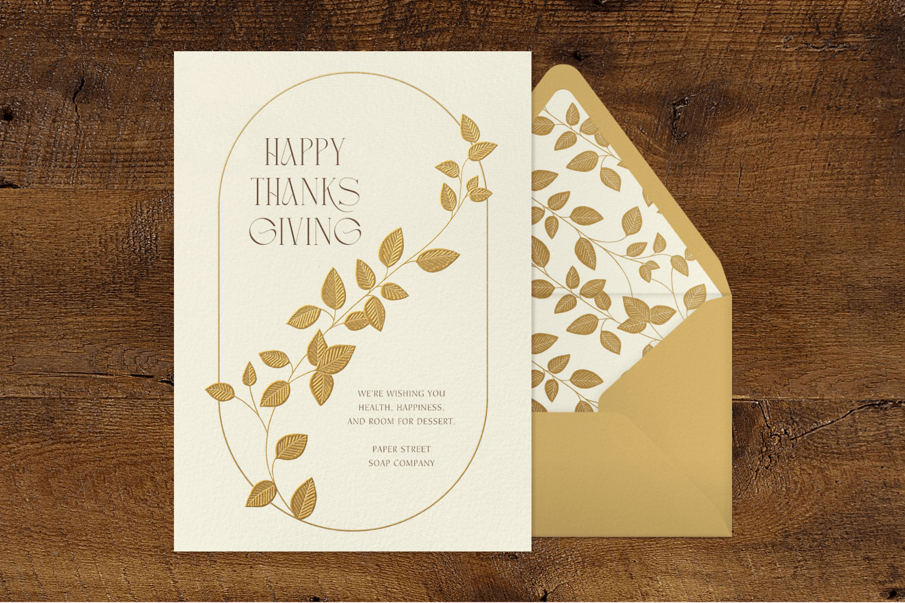A card with a gold oval border and gold leaft vine beside a matching envelope says “Happy Thanksgiving.”