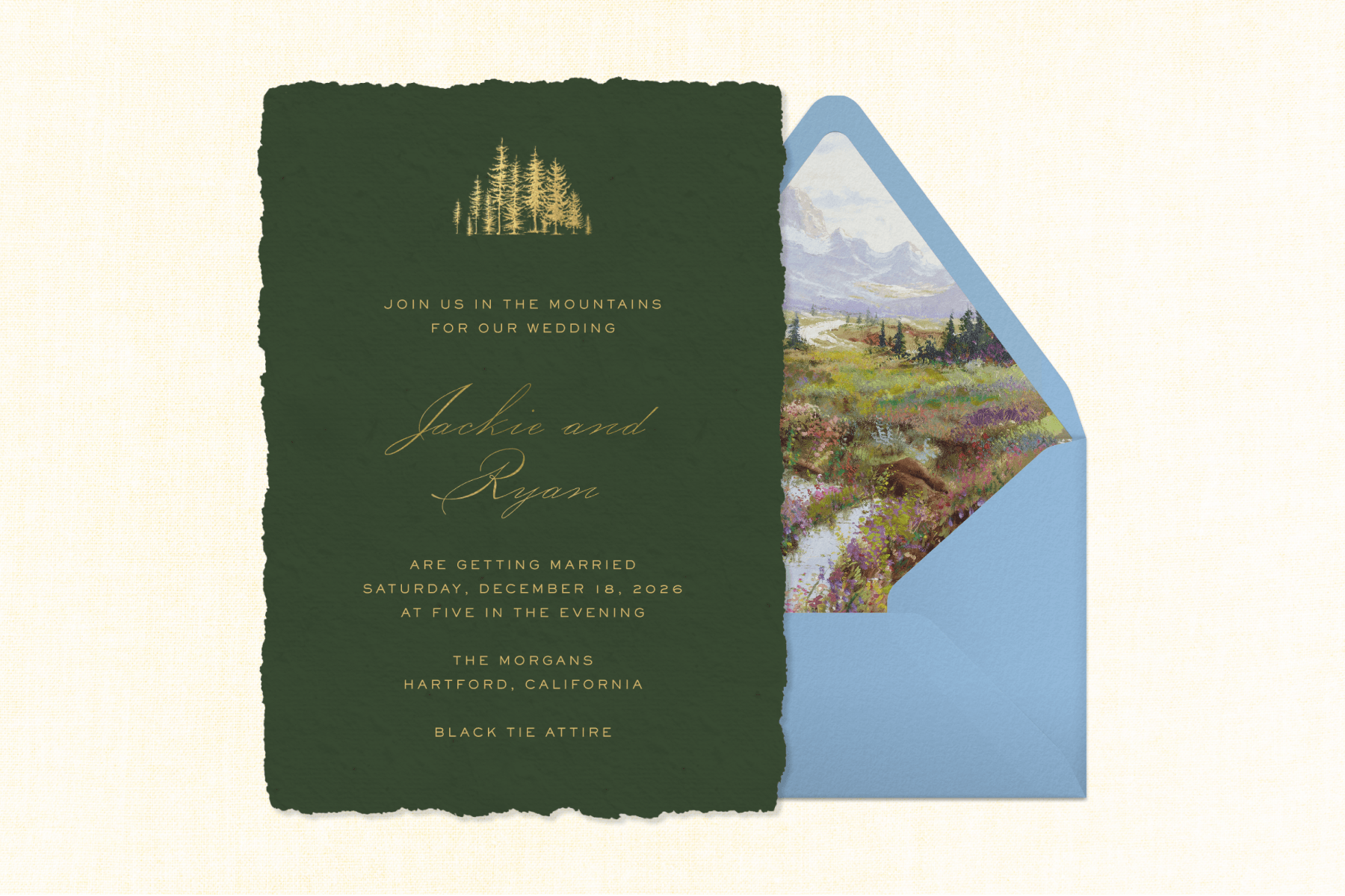 A forest-green, mountain-themed wedding invitation sits to the left of a light blue envelope with a wildflower field interior, set against a textured cream-colored backdrop.