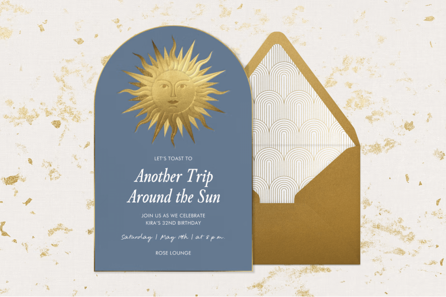 A domed navy invitation with a gold sun with a face, on a gold envelope with swirl liner, on a marble backdrop.