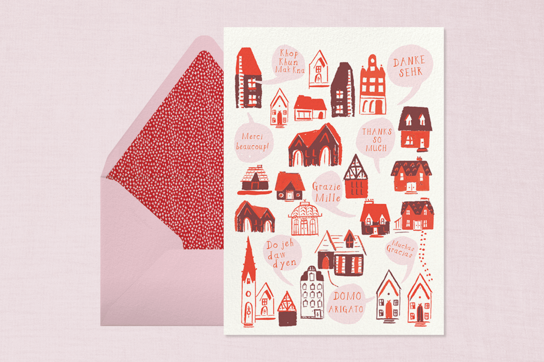 A thank you card with small red paintings of various styles of homes, and words of gratitude in various languages beside a pink envelope with red and white polka dot liner.