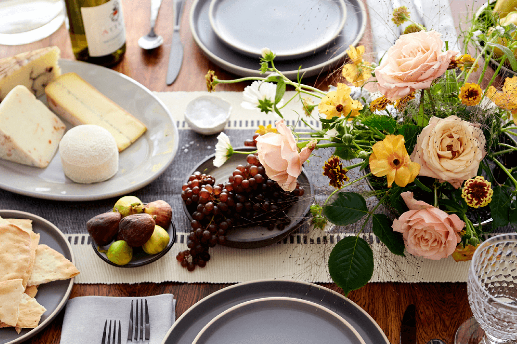 Close up of table settings including a floral centerpiece and some fruit and cheese.