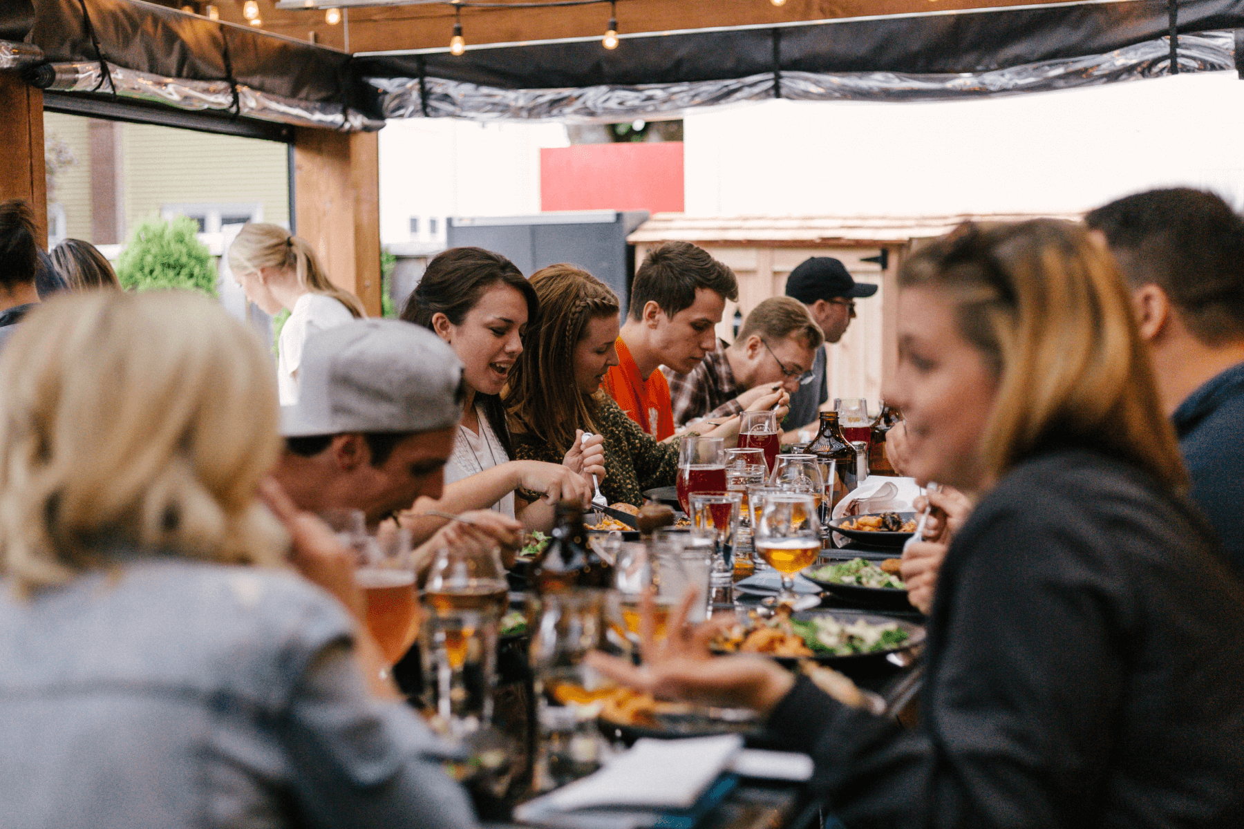 Angled view of several young professionals enjoying dinner and drinks on a covered rooftop.