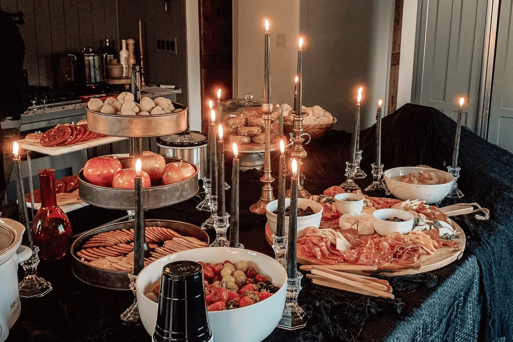 An eerie tablescape with black tapered candles and lots of savory snack options like charcuterie and crackers.