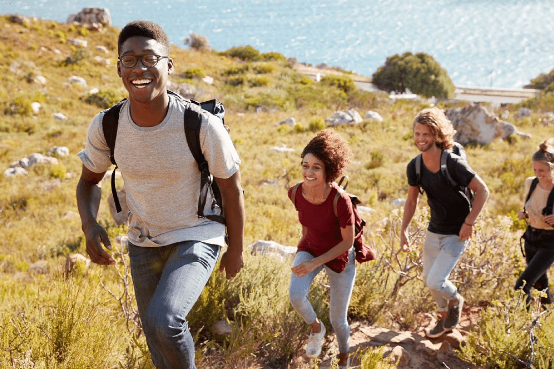 Four young people hike up a grassy hill with a body of water behind them in the distance.