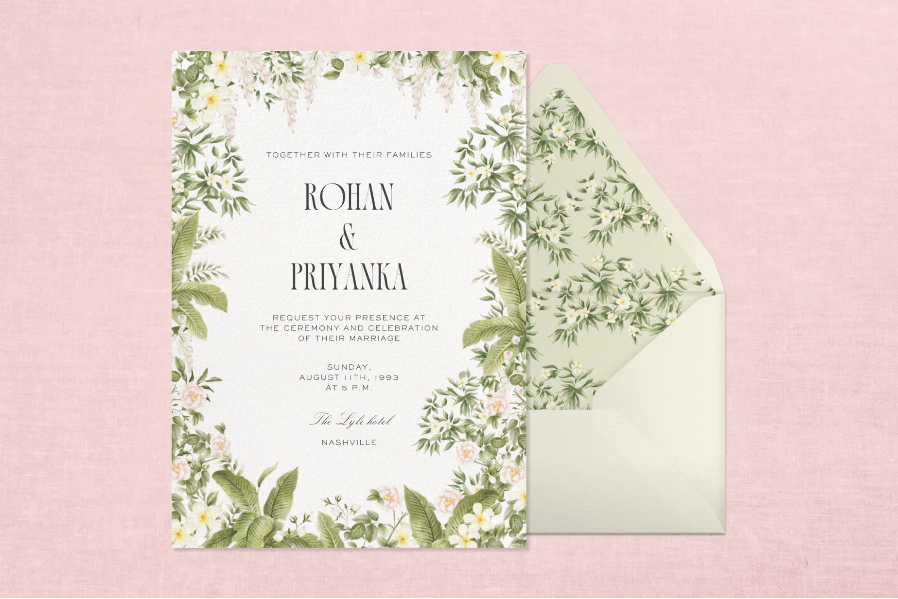 A floral wedding invitation featuring pink flowers and green leaves, paired with a light green envelope and matching floral envelope liner on a light pink background.
