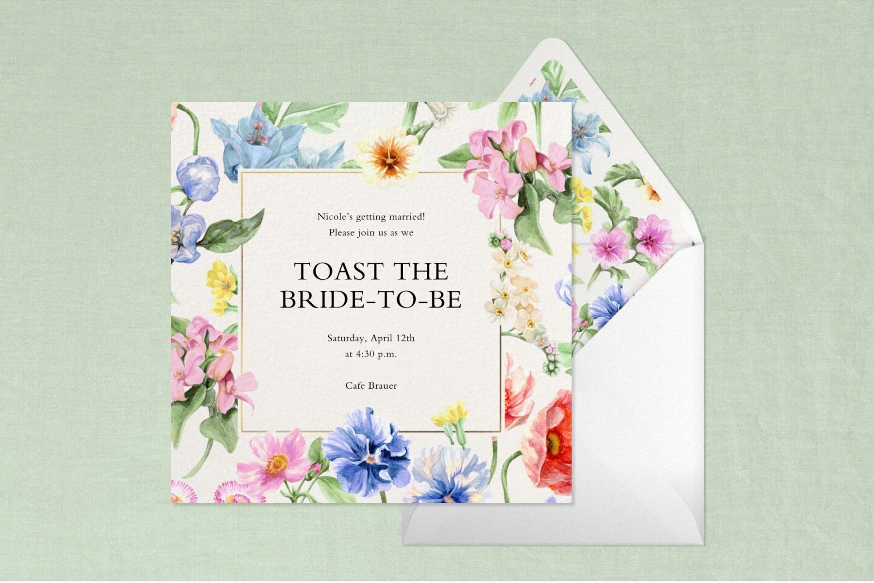 A white invitation with text reading, ‘Toast the bride-to-be’ with a multicolored floral border sits over a white envelope with a matching floral liner on a green background.