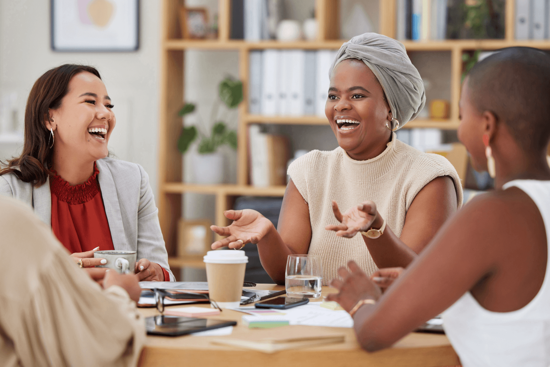 Four women sitting at a table with drinks and notebooks talking and laughing.