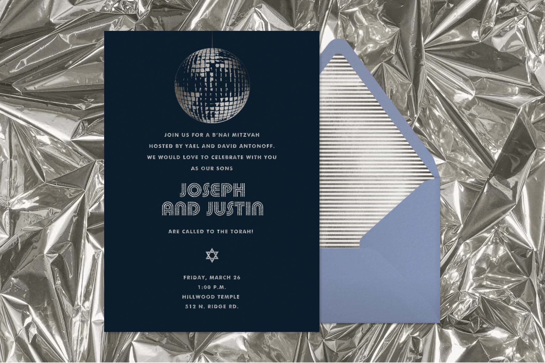 A dark gray invitation with light gray silver lettering and a disco ball at the top, atop a light blue invitation with silver stripes; a backdrop of crinkled silver.