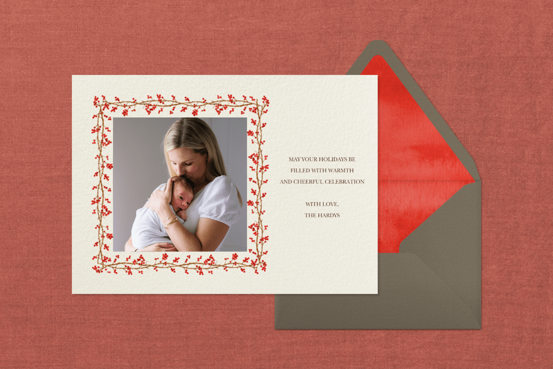 A horizontal photo holiday card with a delicate winter berry border, featuring a mother kissing her newborn baby.