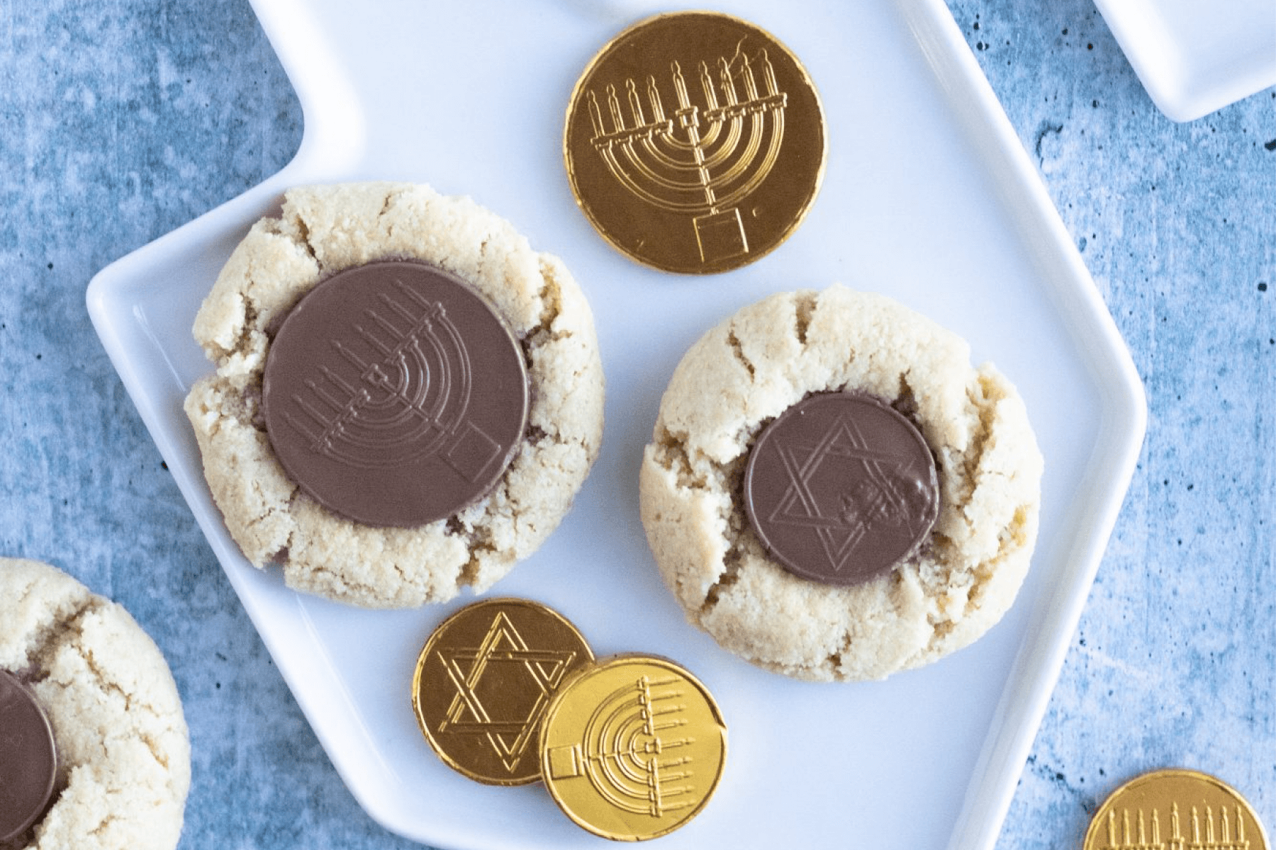 Peanut butter blossoms with gelt decorations on a dreidl-shaped white plate.