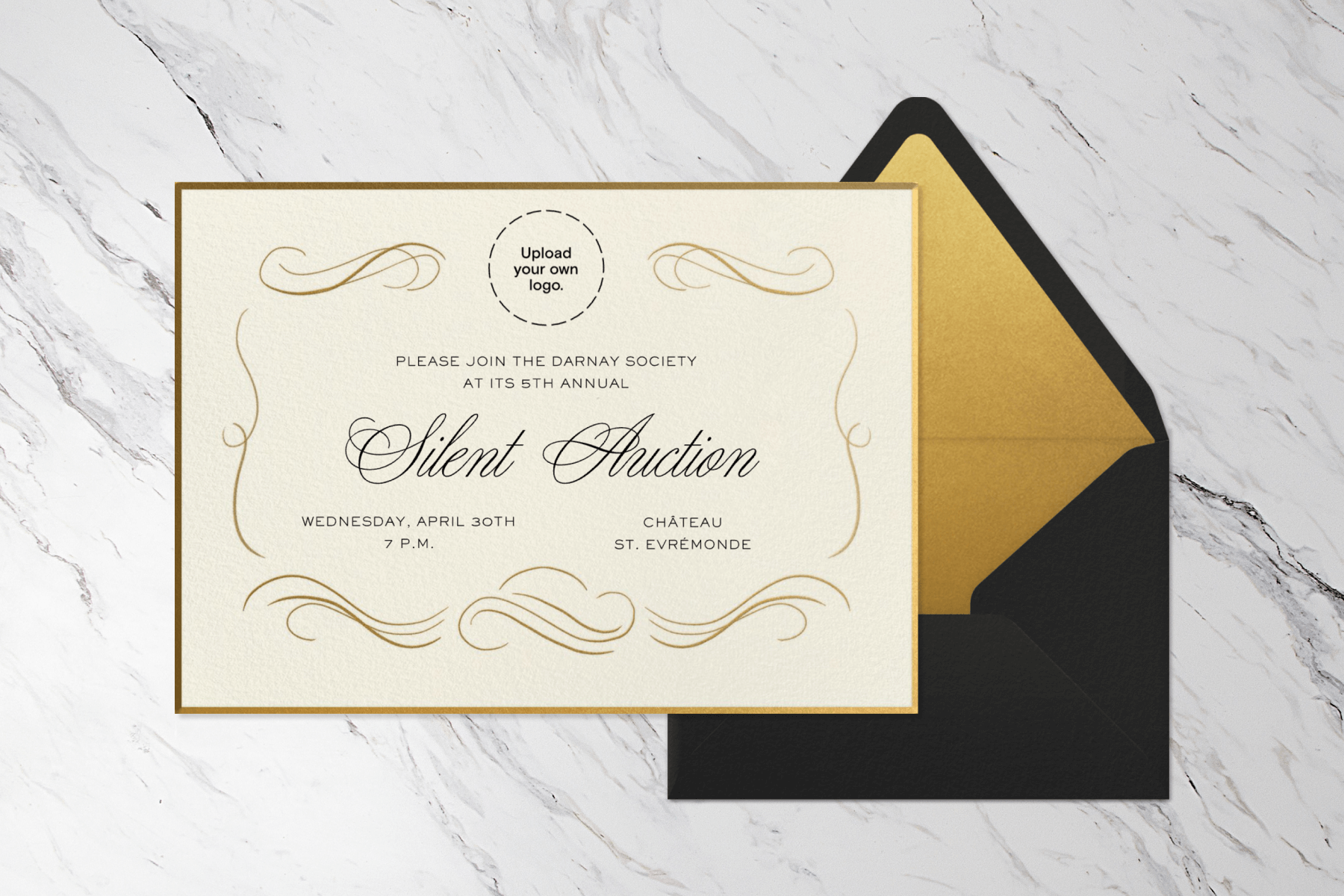 An invitation to a silent auction with cursive script and gilded embellishments showing the ability to upload your own logo, sits on a black envelope with a gold liner, all on a black and white marble backdrop.