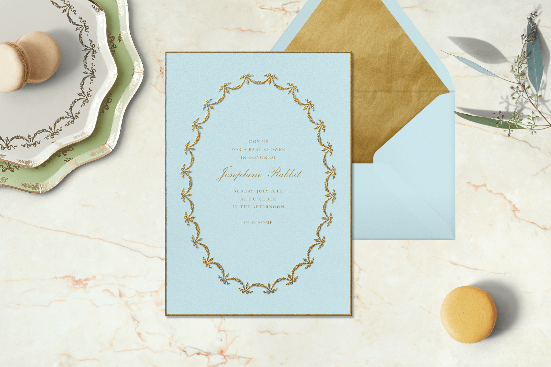 A blue Ladurée invitation surrounded by macarons and plates.
