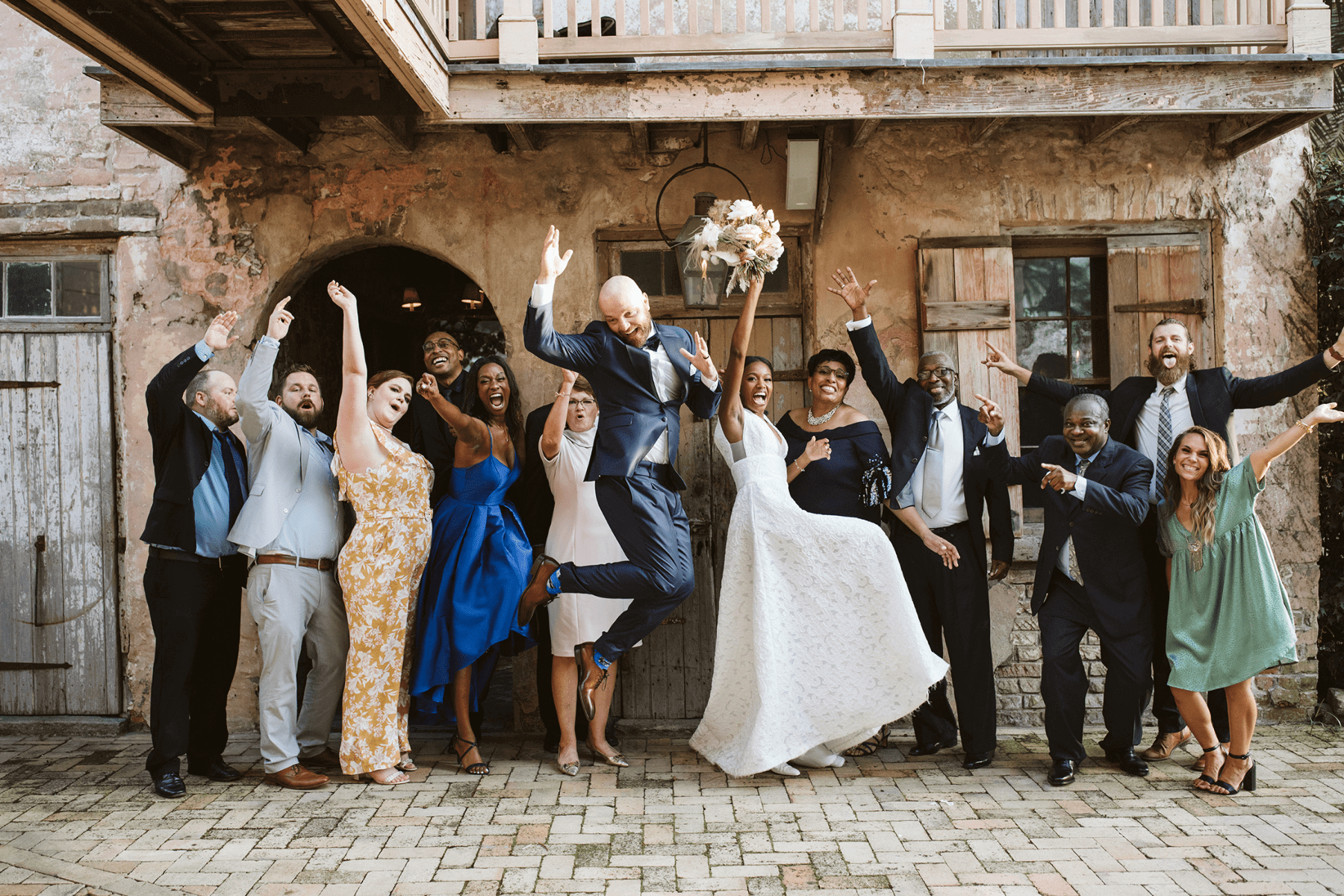 A happy couple and guests posing with their hands raised at their wedding.