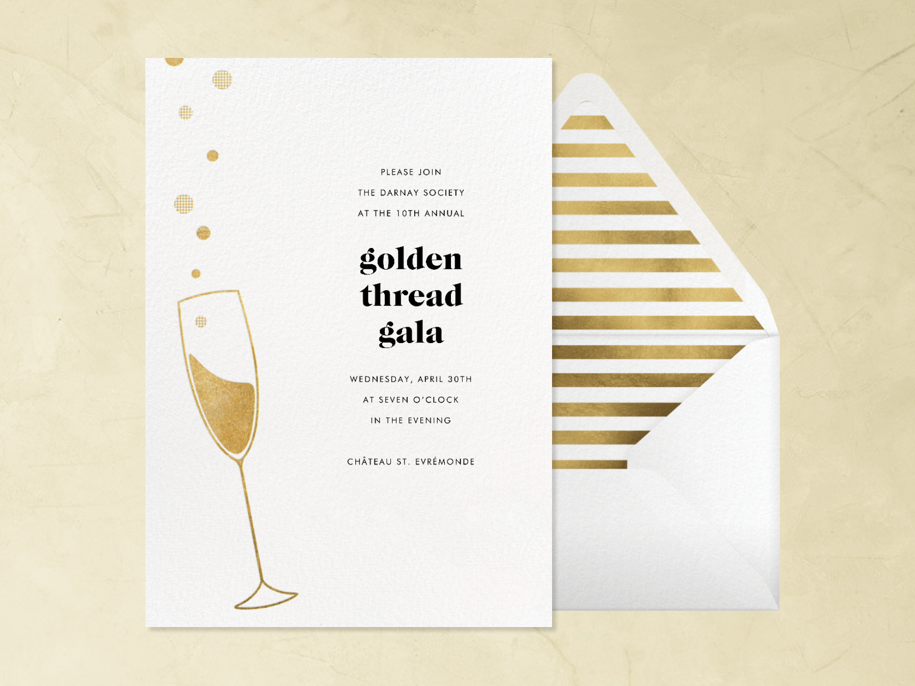 An invitation for the Golden Thread Gala shows a gold Champagne flute with bubbles floating out of it, beside a white envelope with gold striped liner.