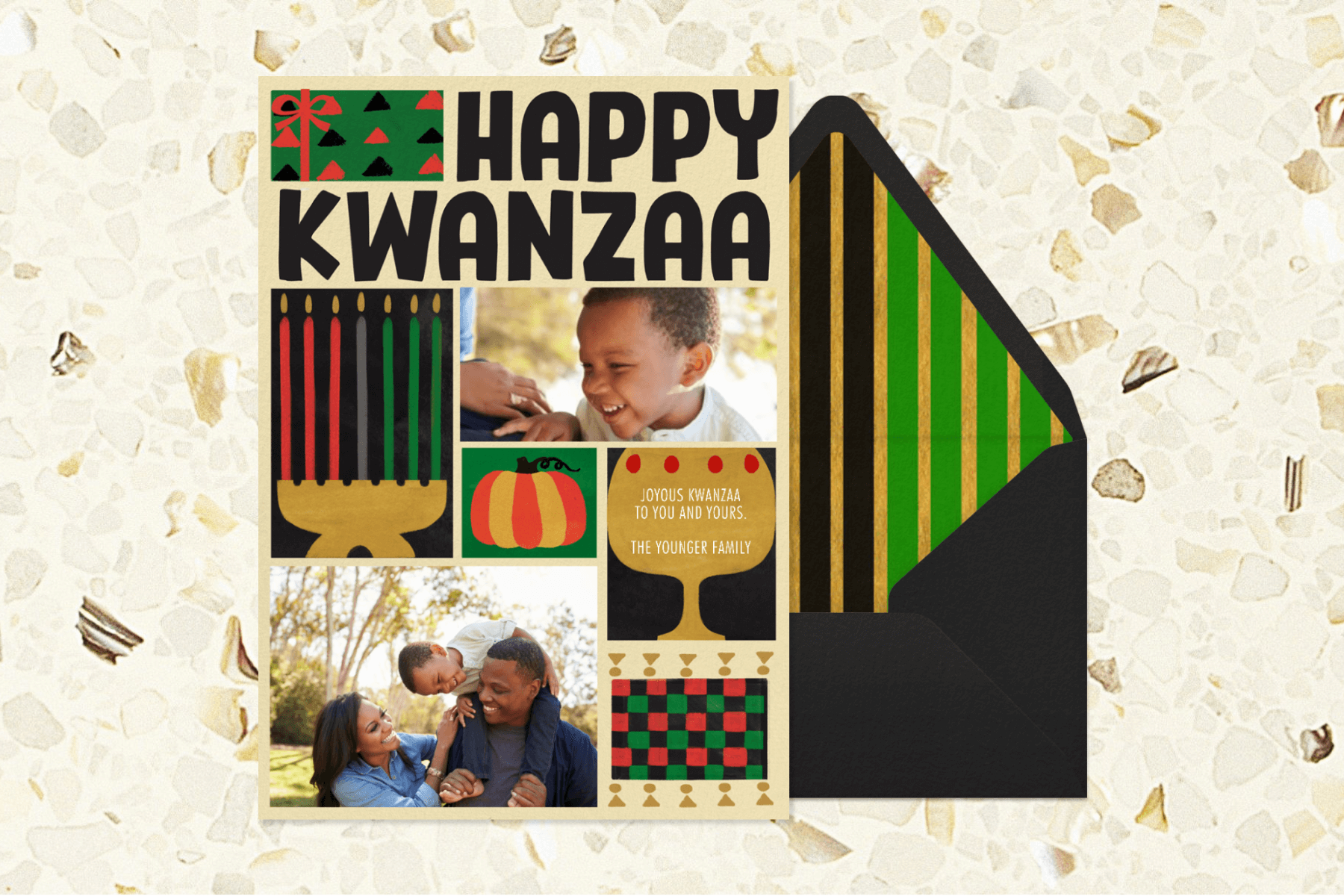 A Kwanzaa card with colorful illustrations of a kinara, a gift, and photos of a young family beside a black envelope with a green, gold, and black striped liner.