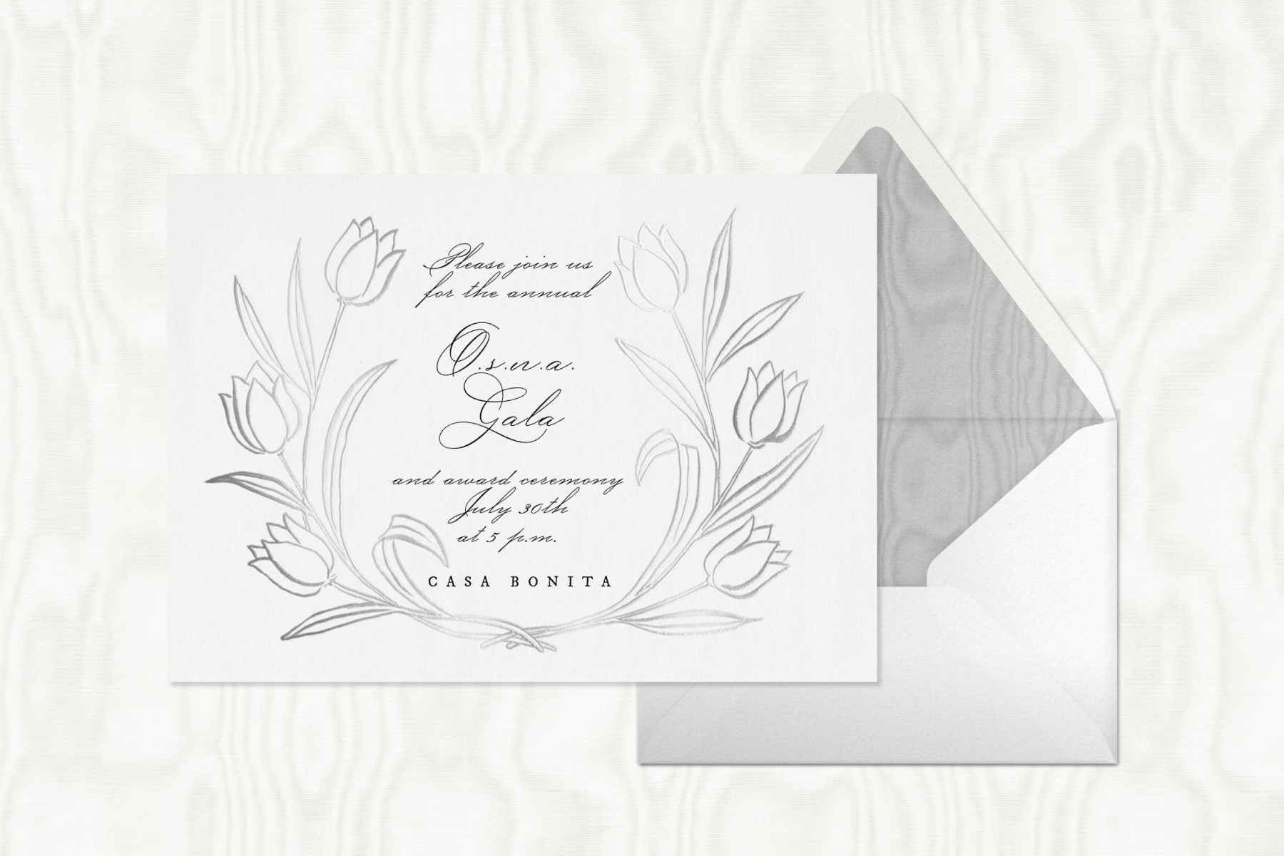 A white floral gala invitation sits to the left of a white envelope with a textured gray interior against a textured white backdrop.