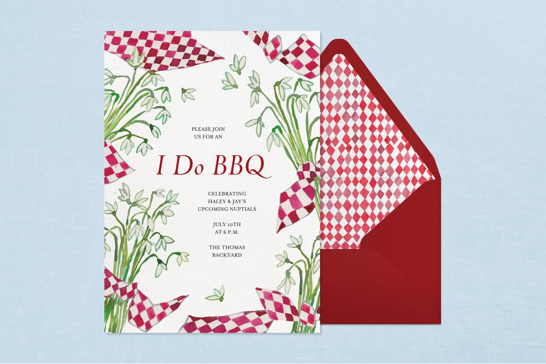 An invitation with text reading, ‘I do BBQ’, illustrations of white flowers, and red and white checkered picnic blankets sits over a red envelope with a checkered liner on a blue background.