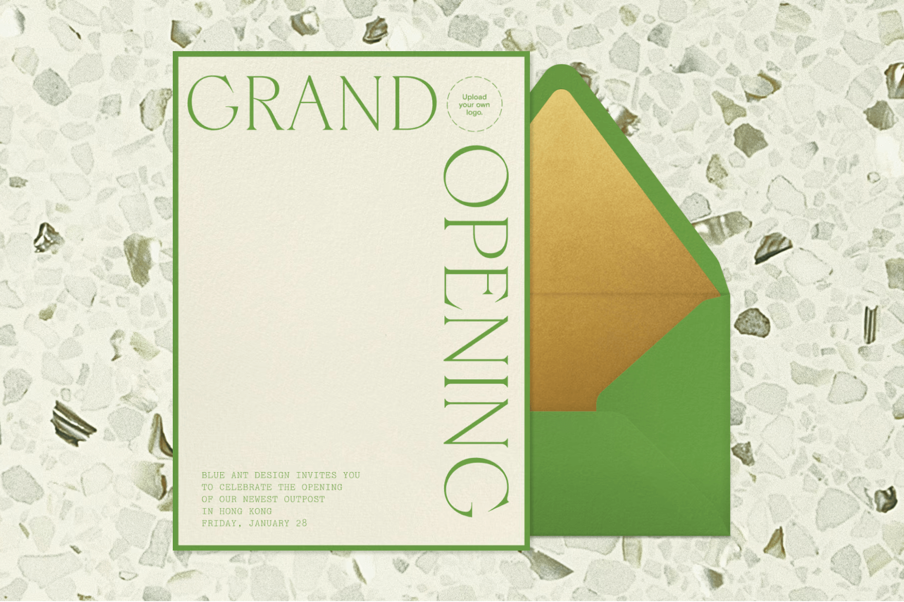 A beige invitation for a grand opening with large green text bordering the design’s top and right sides, next to a green envelope, over a speckled white and dark green background.