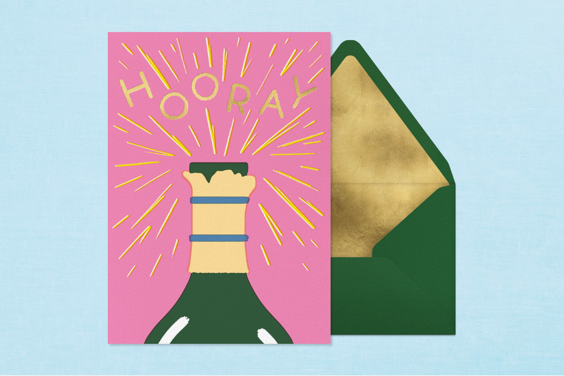 A card featuring an illustration of a popping champagne bottle and text that reads ‘HOORAY’ paired with a green envelope and gold foil envelope liner.