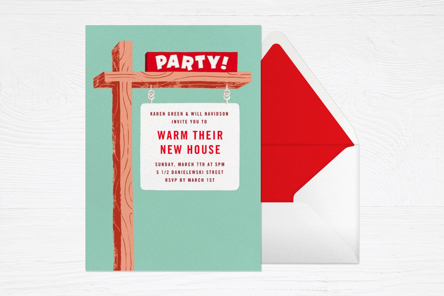 A green housewarming party invitation on a white wood backdrop with a red-lined envelope resembles a “sold” sign in front of a house with the words “warm their new house” on the hanging sign.
