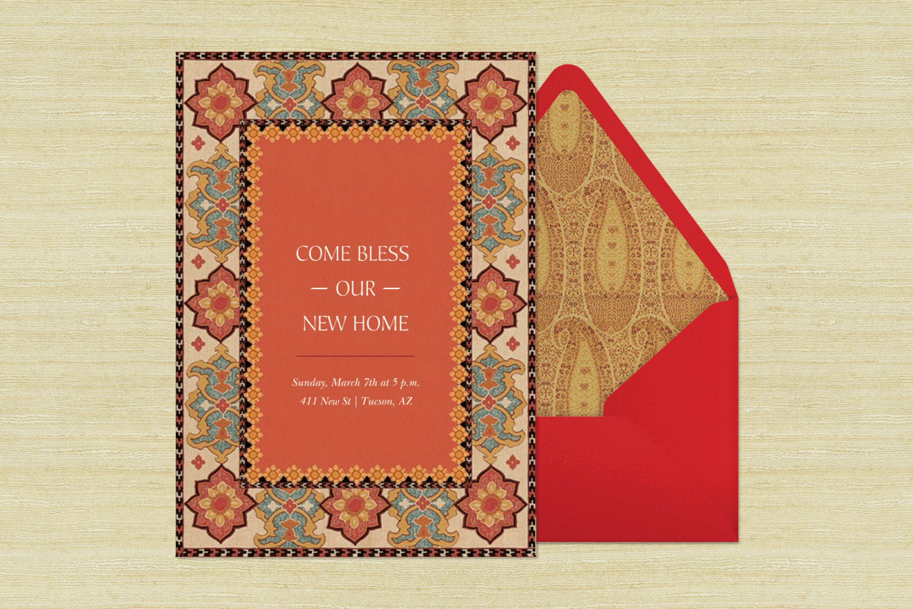 An invitation for a housewarming party reads “Come bless our new home” with a faded bohemian pattern around the border and muted orange in the middle beside a red envelope with a faded yellow paisley print liner.