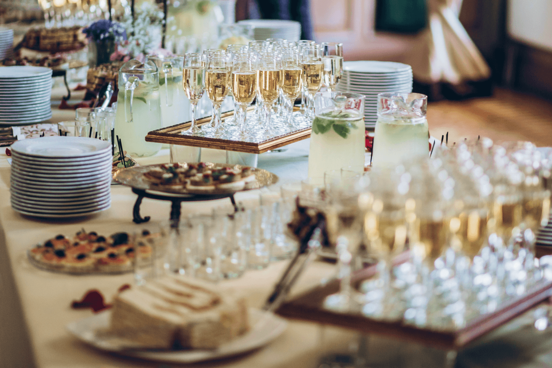 A banquet table is covered in stacked dishes, Champagne flutes, and passed hors d'oeuvres ready to be served.
