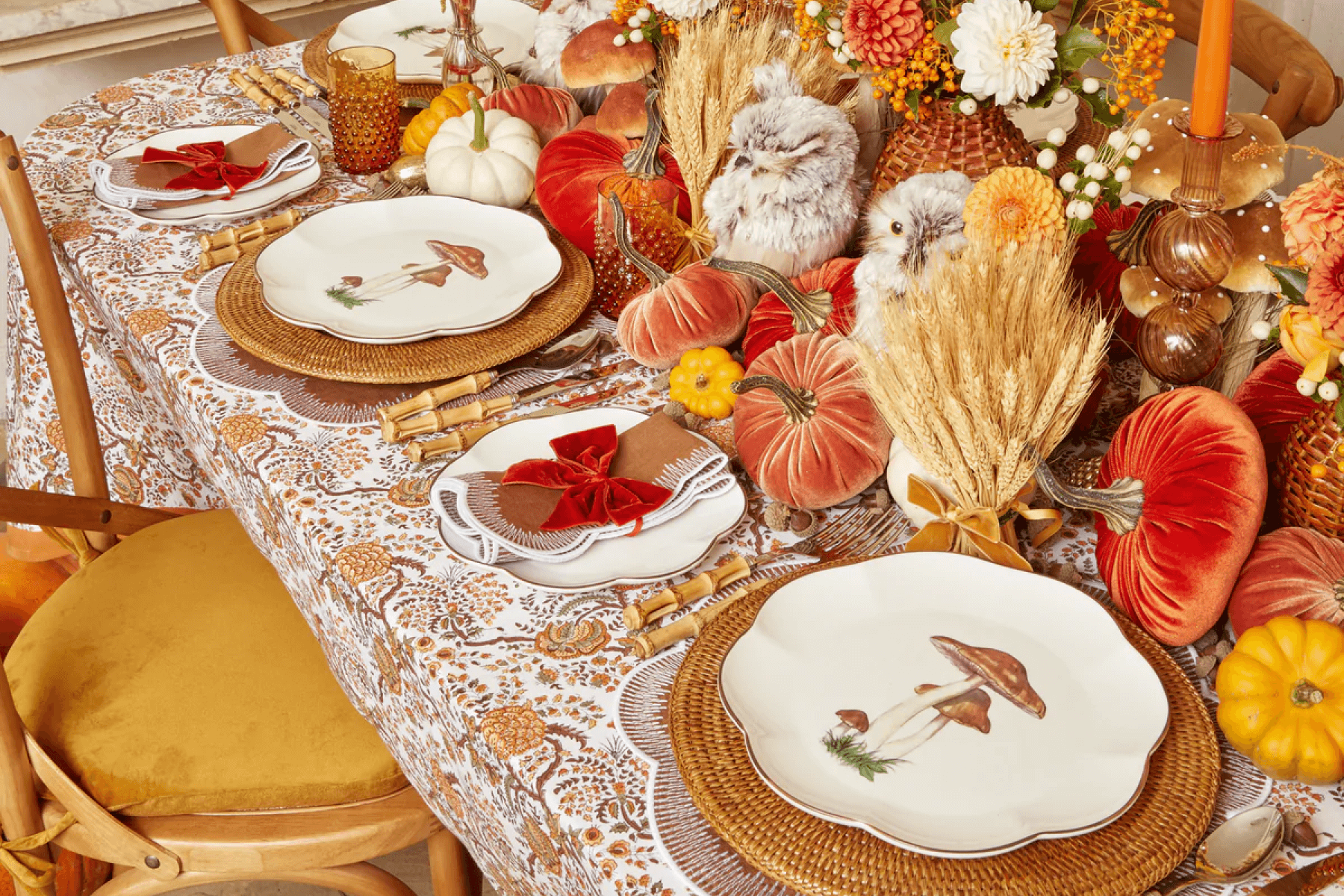 An image of an autumnal table setting replete with velvet pumpkins, stuffed owls, wheat bundles, and mushroom plates.